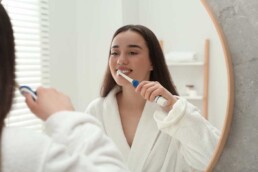 Woman brushing teeth in bathroom mirror.